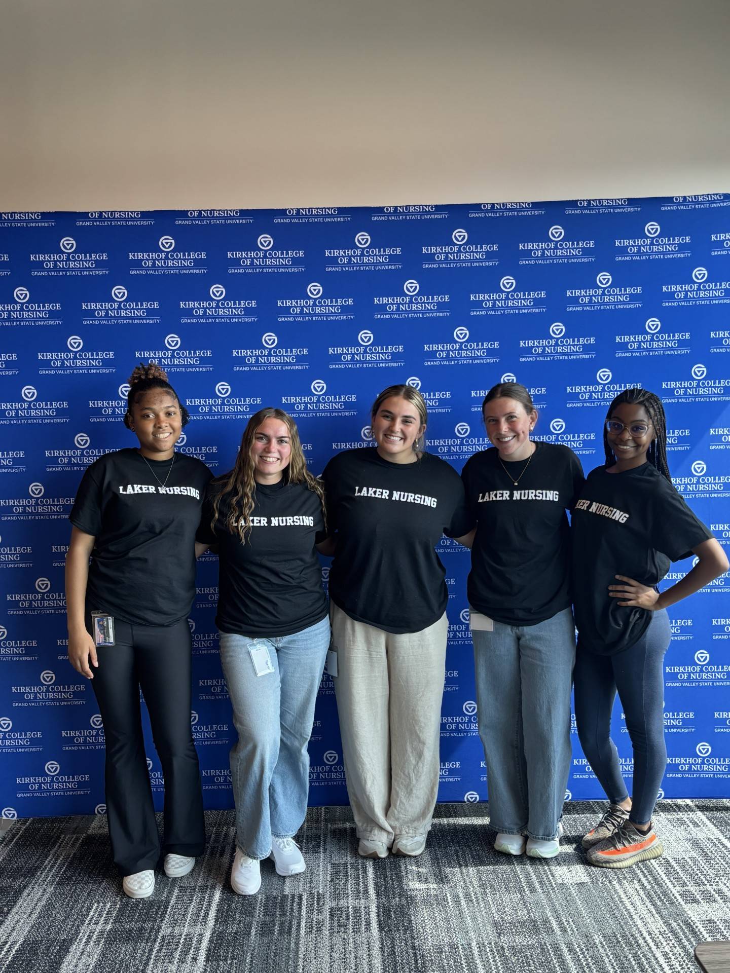 5 students in "Laker Nursing" t shirts standing in front of blue Kirkhof College of Nursing banner